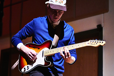 Guitarist with a blue shirt and hat plays on stage
