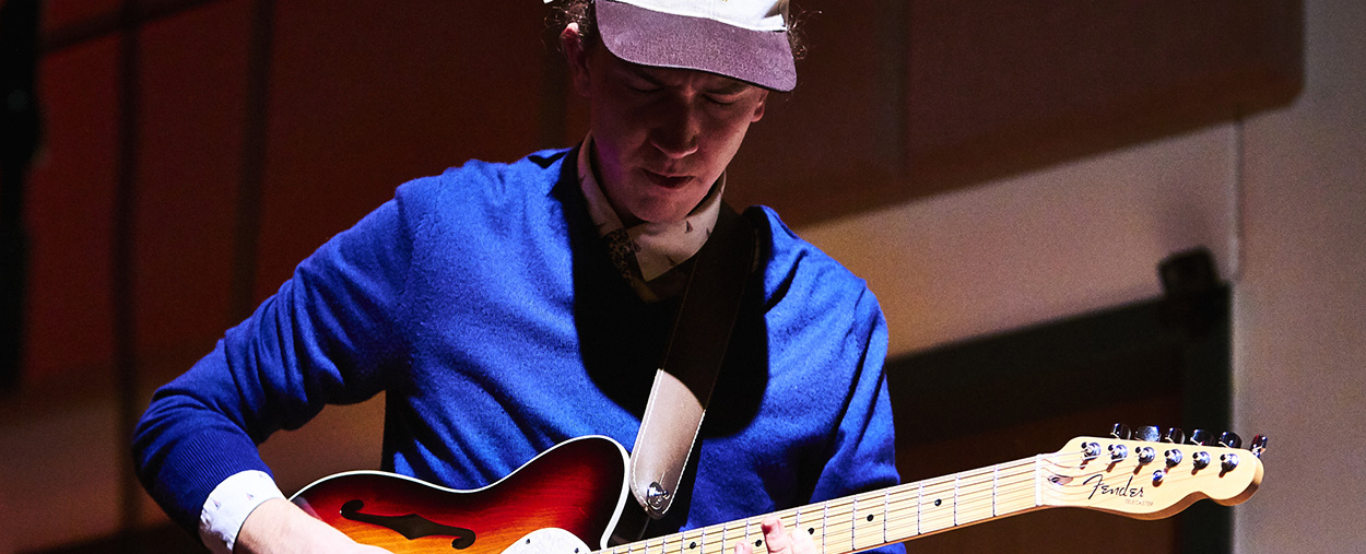 Guitarist with a blue shirt and hat plays on stage